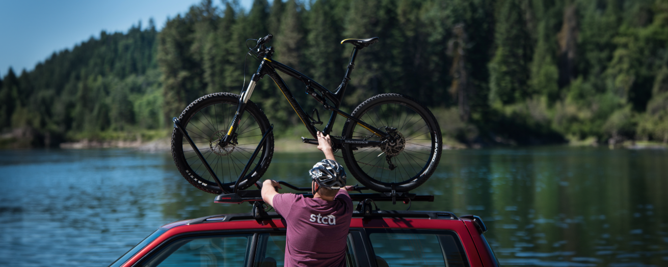 Photo of a man in an STCU shirt putting a mountain bike on top of an SUV