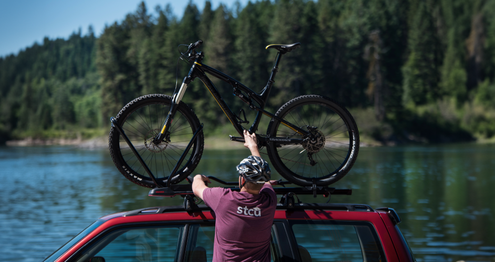 Photo of a man in an STCU shirt putting a mountain bike on top of an SUV