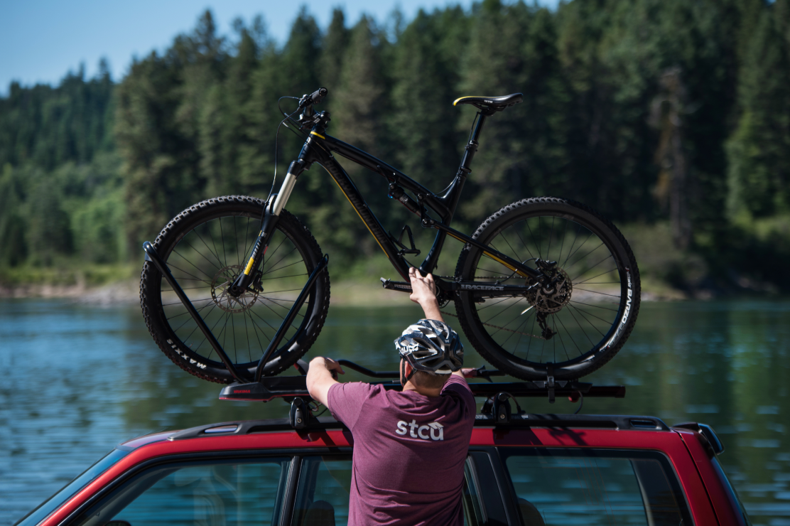 Photo of a man in an STCU shirt putting a mountain bike on top of an SUV